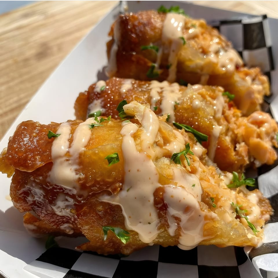 Three golden-fried Mexican taquitos drizzled with creamy sauce and fresh cilantro in a checkered basket.