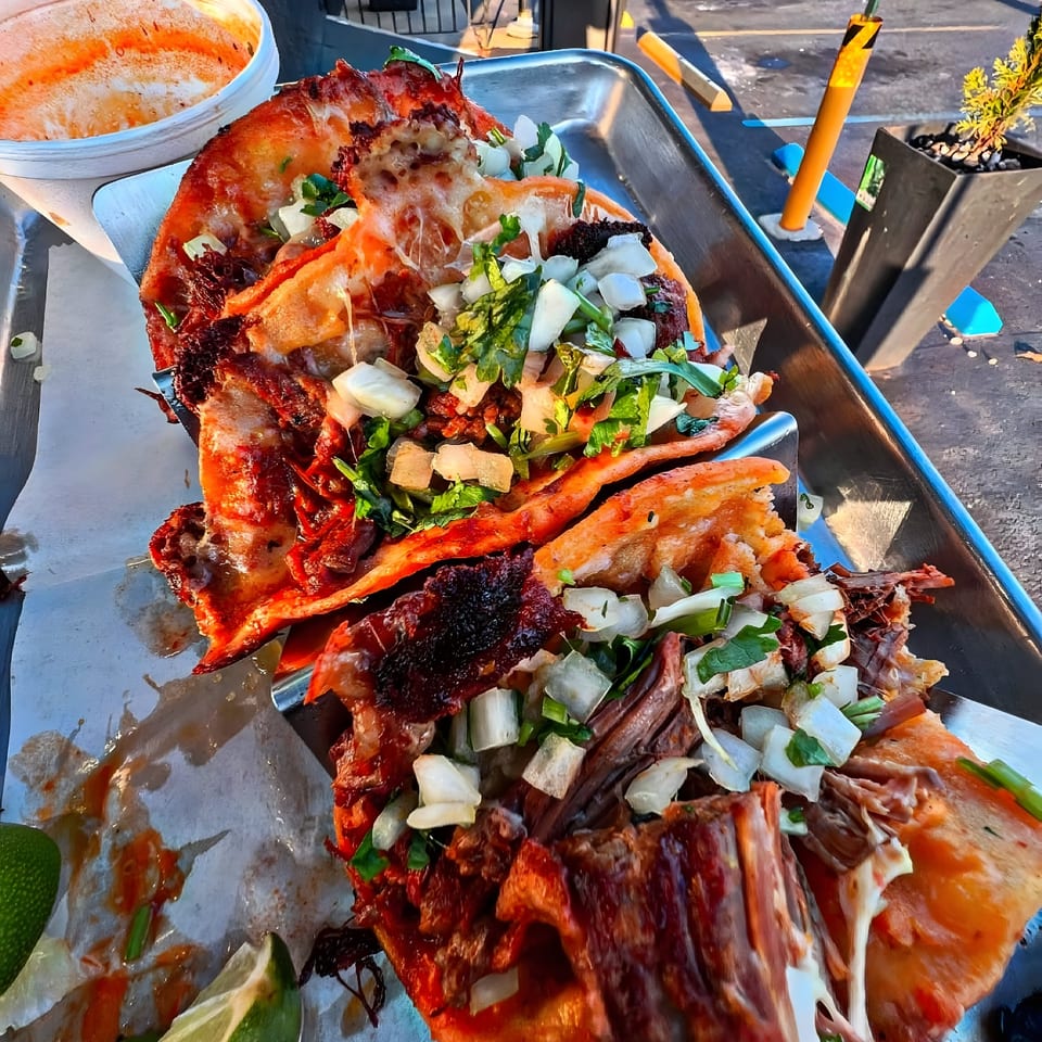Close-up of Tacos Mexiko's birria tacos with melted cheese, onions, and cilantro on a metal tray.