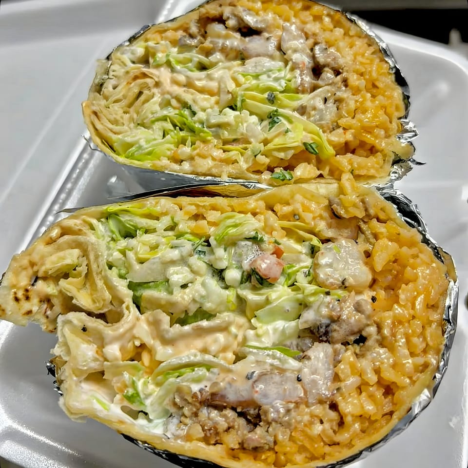 Two halves of a large burrito, filled with rice, meat, lettuce, and creamy sauce, wrapped in foil.