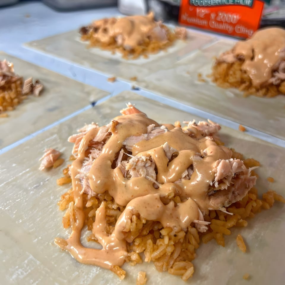 Several Mexican burritos with rice, shredded chicken, and creamy sauce on tortillas.