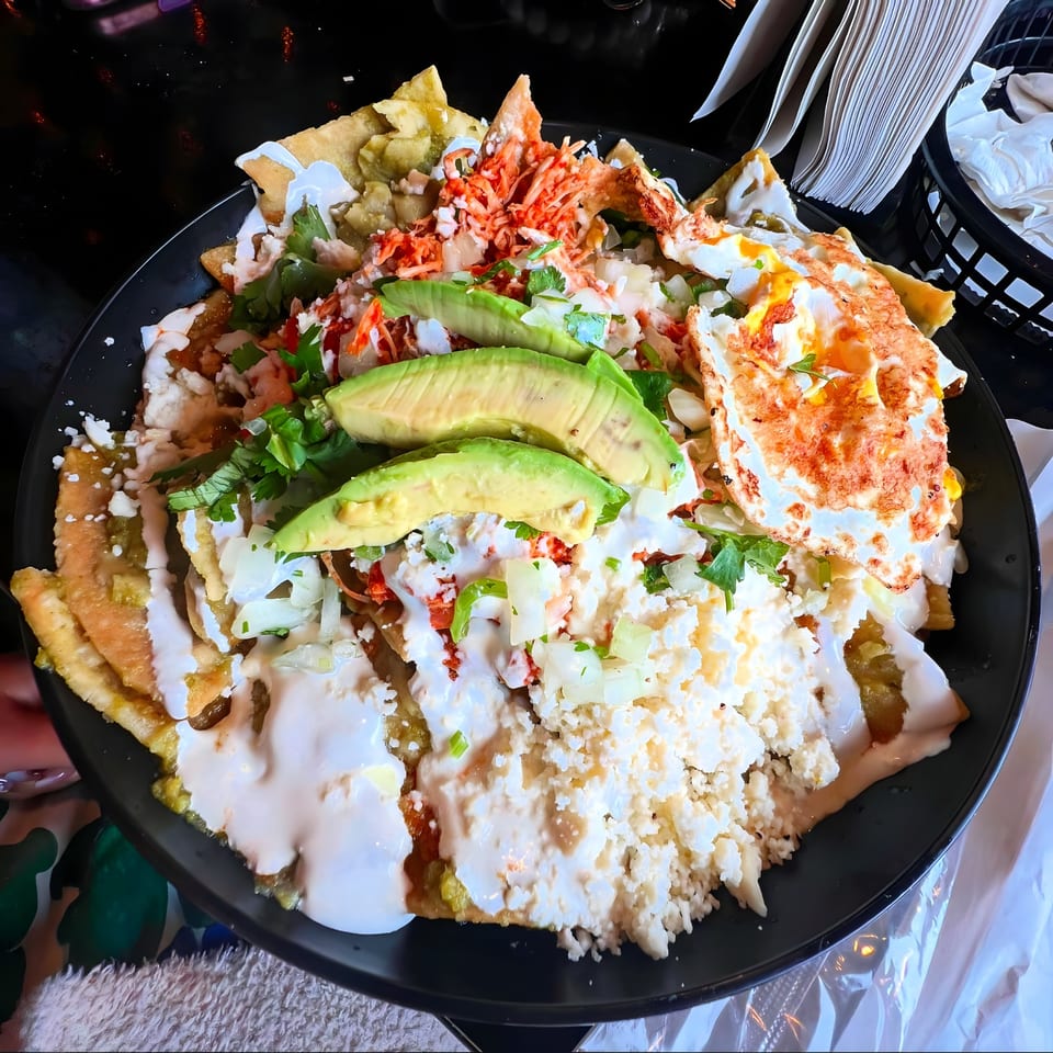 A large plate of Tacos Mexiko chilaquiles with avocado, cheese, and a fried egg.